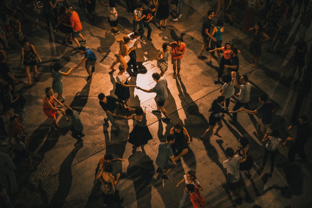people holding hands dancing in concentric circles on dimly lit dance floor