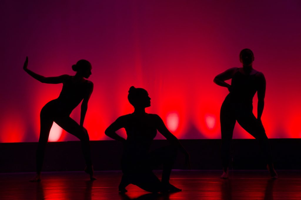 silhouette of three women dancing in front of a red curtain 