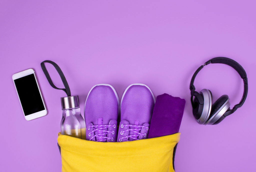 yellow dance bag with shoes, water bottle and headphones coming out on purple background