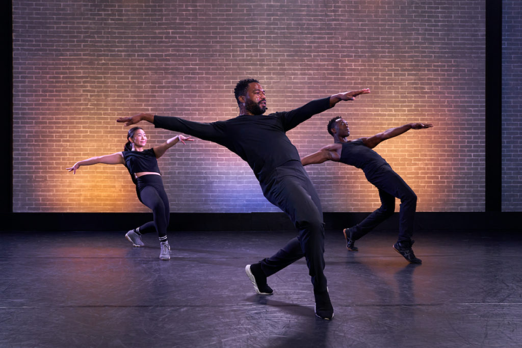 broadway dancer grasan kingsberry and assistants in all black lunging forward with arms out 