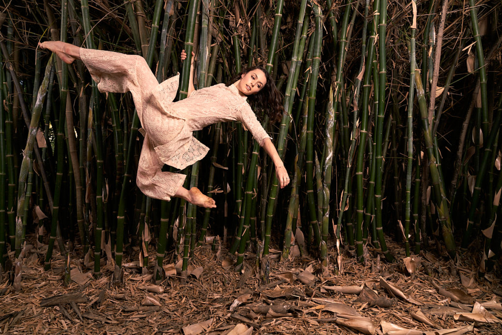 dancer kathryn mccormick holding onto a bamboo tree while leaping 