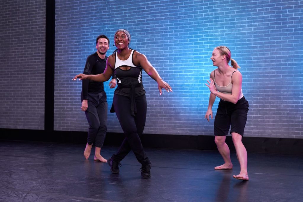 three dancers laughing and stepping around in a studio 