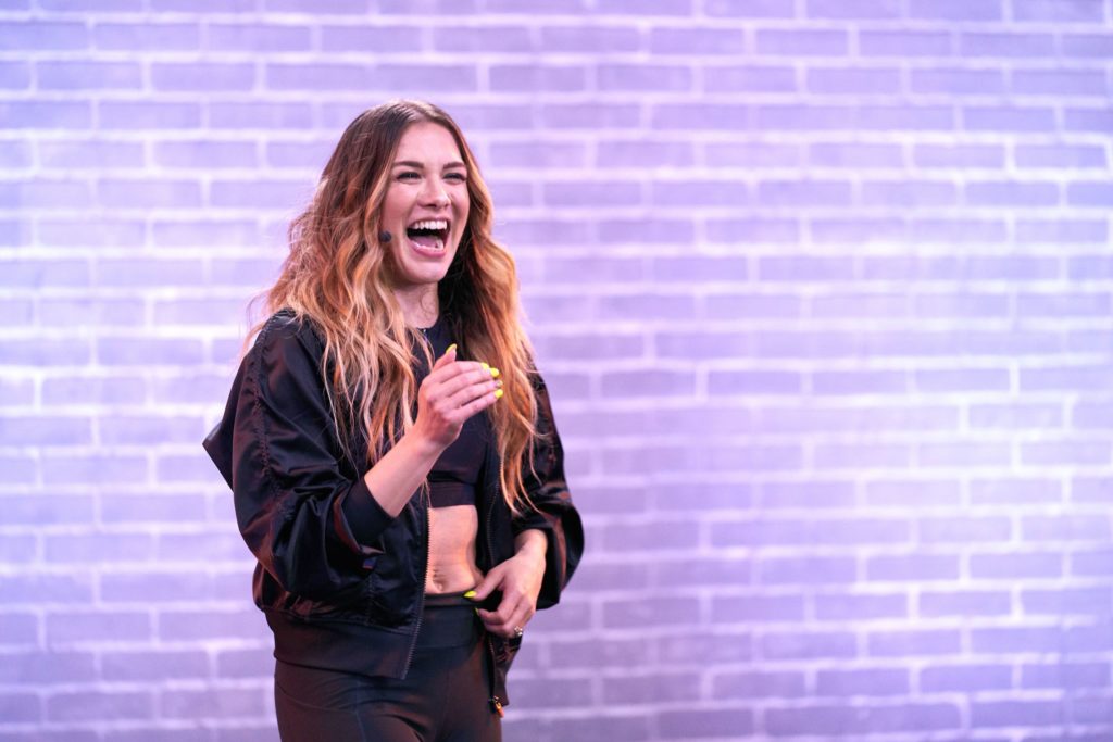 dancer allison holker smiling and clapping in front of a purple brick wall