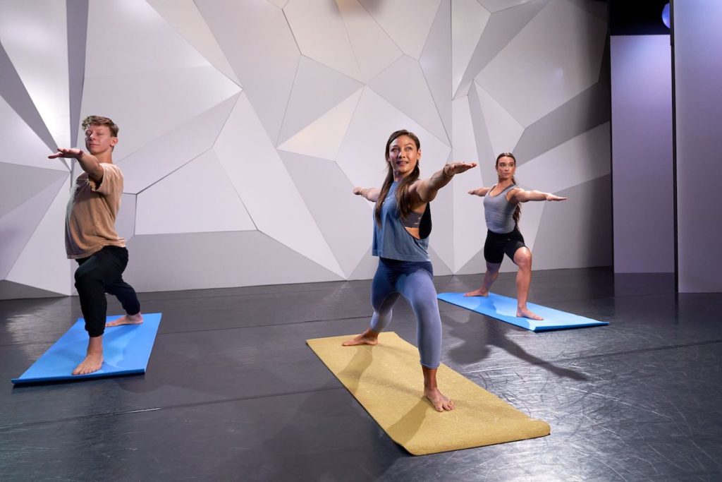 3 dancers in a warrior two yoga pose on yellow and blue mats