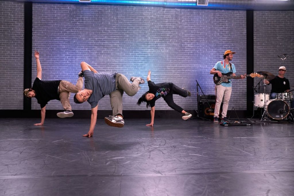three breakdancers balancing on one arm and kicking their legs into the air