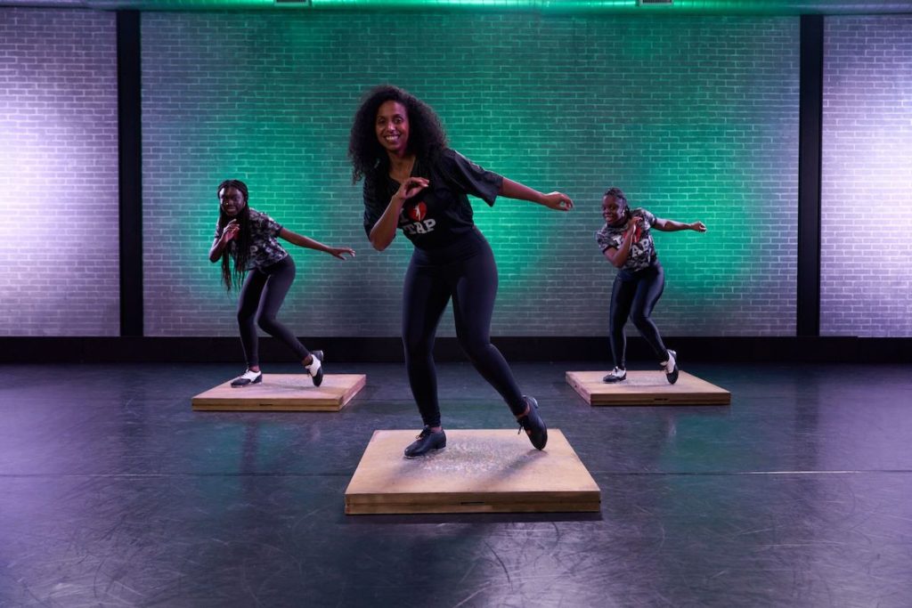Chloe arnold at cli studios with 2 other dancers stadning on wood boards with arms out to the side. 