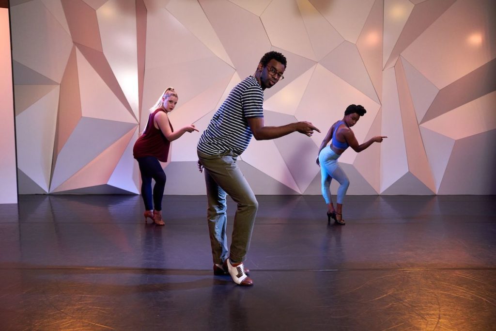 Dom kelley with 2 other female dancers standing with knee popped and pointing finger at cli studios.
