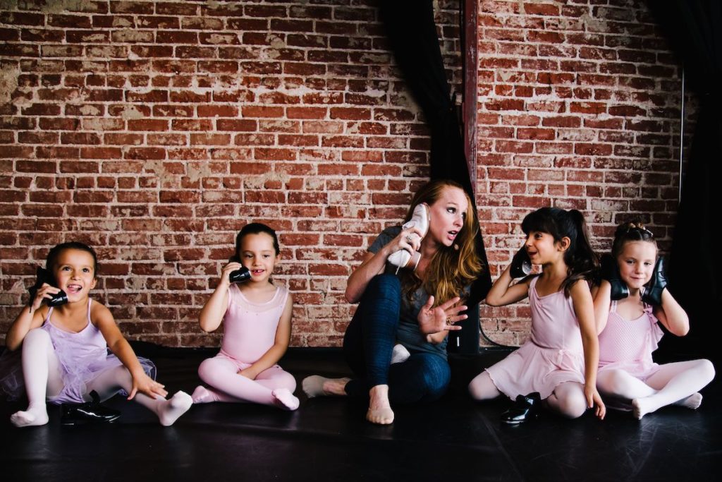 dance teacher julie kay stallcup sitting in a studio with four pre-school dancers pretending to use their tap shoes as phones