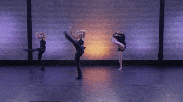 3 female dancers dressed in black performing a fan kick infrotn of brick wall. 