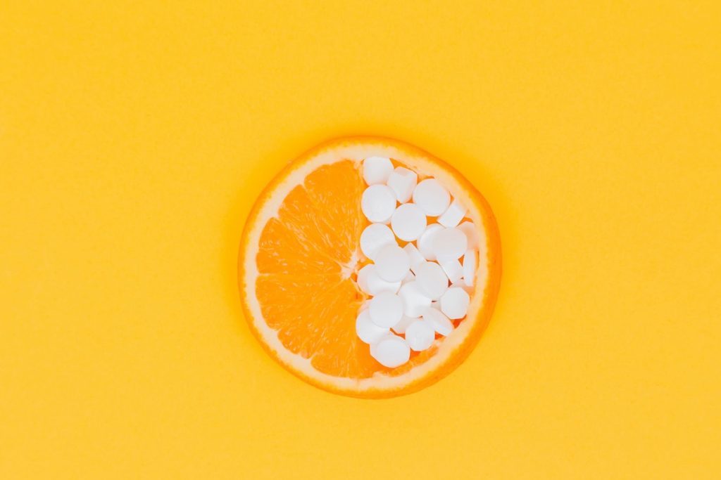 orange slice and vitamin c supplement against an orange background