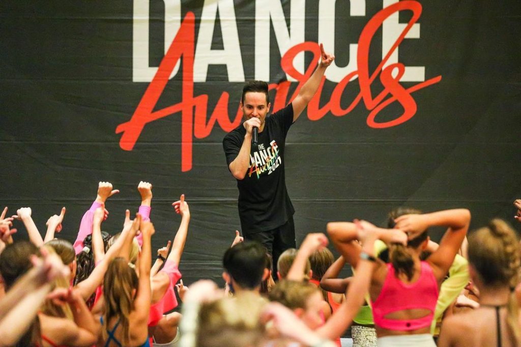dance instructor colby shinn onstage talking to a group of young dancers