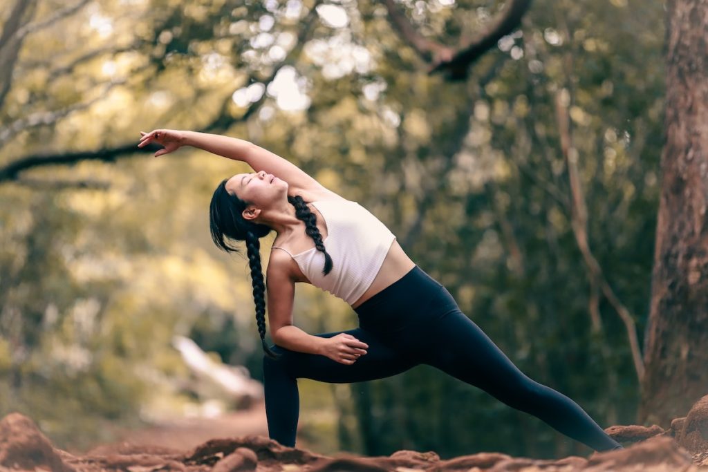 woman outside in black leggings and a white tank top in extended side angle yoga pose