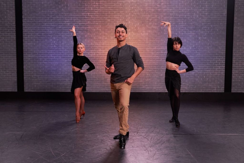 dancer paul karmiryan wearing slacks, a button-up, and dress-shoes while he teaches class with two female assistants in black skirts, crop tops, and heels