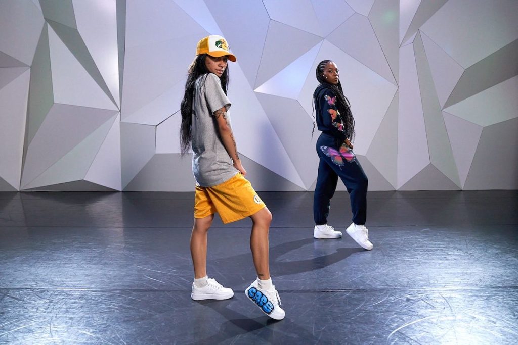 dancer ysabelle capitule teaching at cli studios wearing basketball shorts, a loose-fitting tshirt, and a baseball cap with her assistant in a sweatsuit 