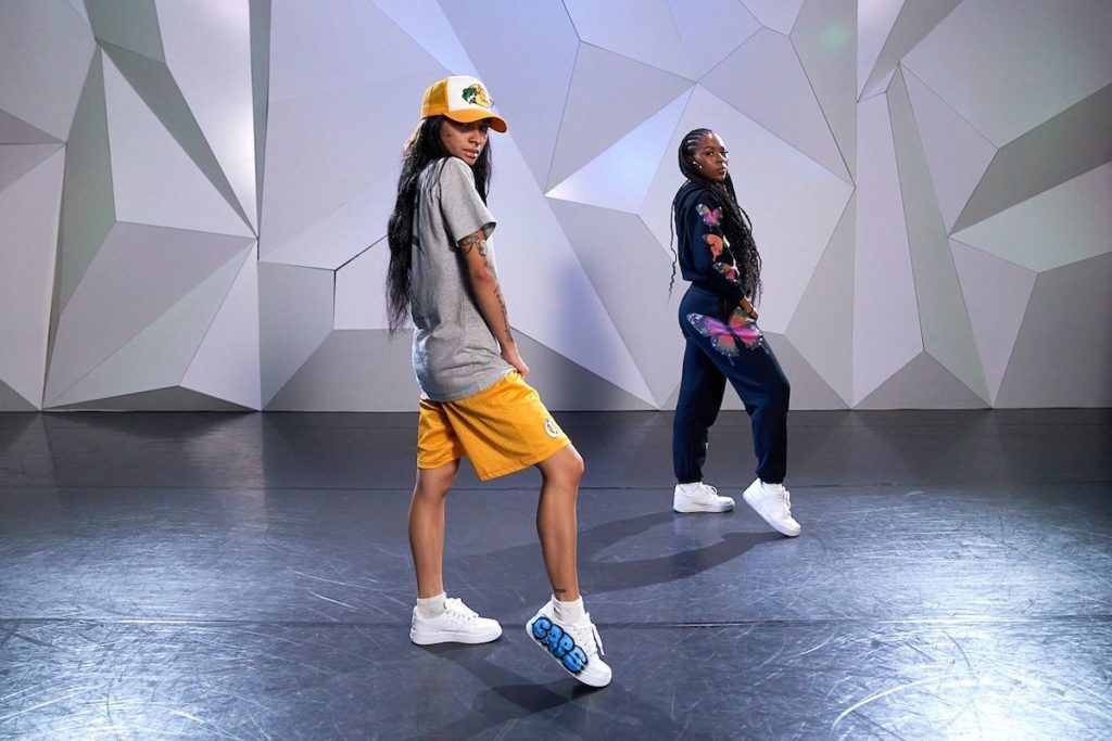 dancer ysabelle capitule teaching at cli studios wearing basketball shorts, a loose-fitting tshirt, and a baseball cap with her assistant in a sweatsuit