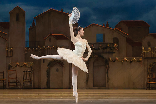 Dancer in arabesque with fan in hand in front of stage scenery