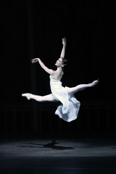 Dancer in oversplits leap in third arabesque wearing a white flowing dress