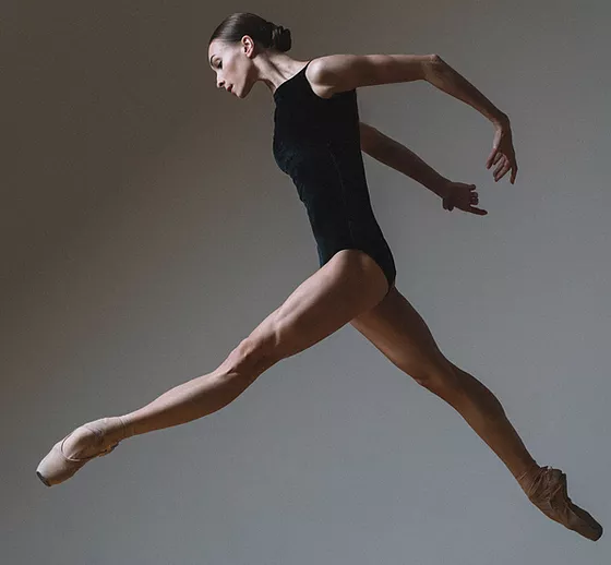 Dancer in black leotard jumping with arms rounded behind back