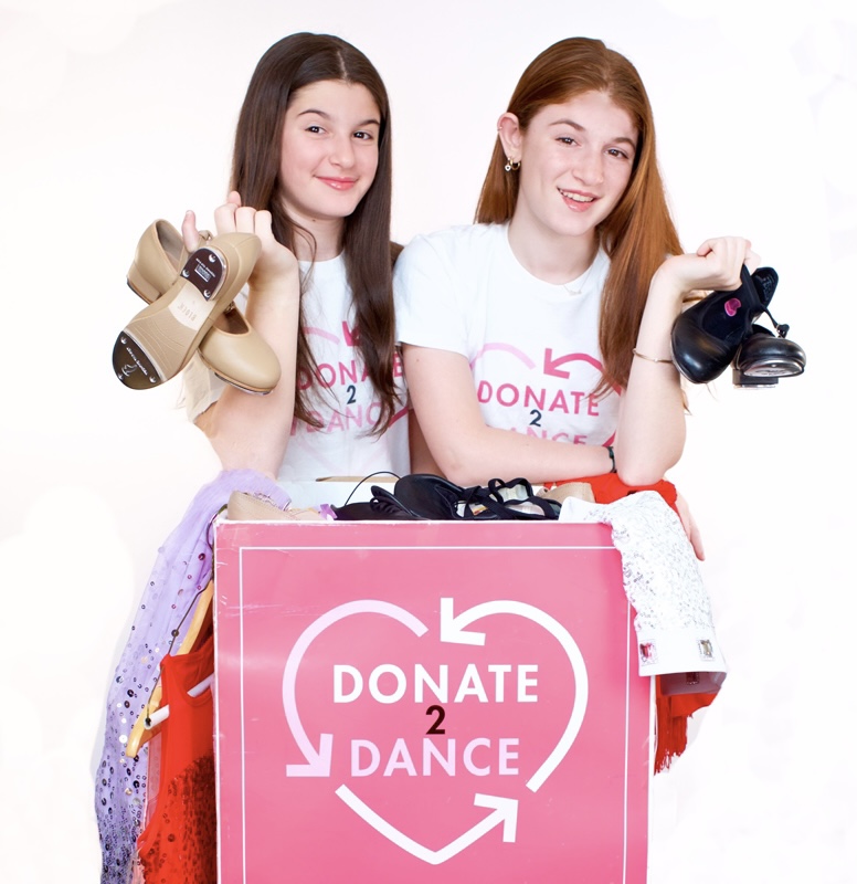 Two girls, Ava and Sophia Paley, holding tap shoes in front of pink box