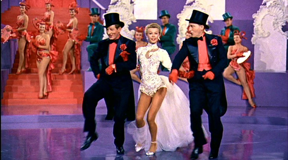 White Christmas the movie, women standing in white dress with men in top hats and tuxs on each arm. 