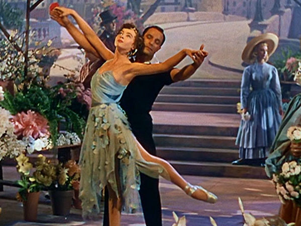 An American In Paris the movie with man standing behind women dressed in floral blue costume and in pointe shoes. 