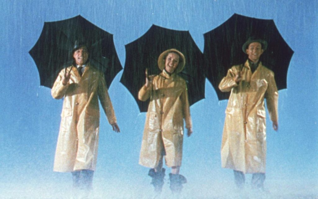 Singin' in the Rain, the movie, 3 people in rain coats and umbrellas. Standing in the rain. 