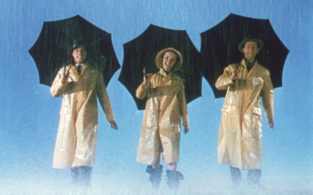 Singin' in the Rain, the movie, 3 people in rain coats and umbrellas. Standing in the rain.