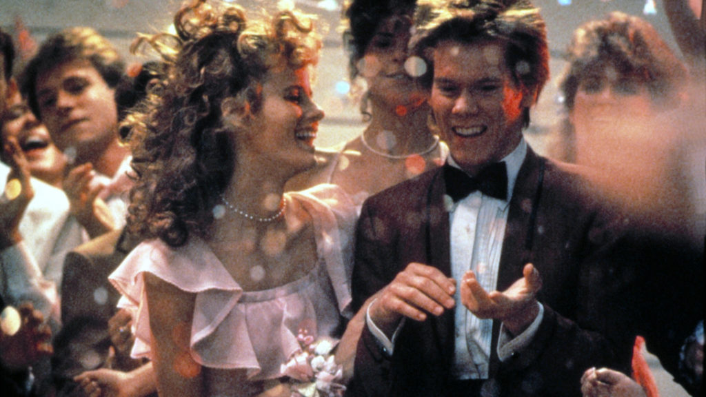 Footloose the movie with women in pink dress standing next to man in tux pointing and laughing.