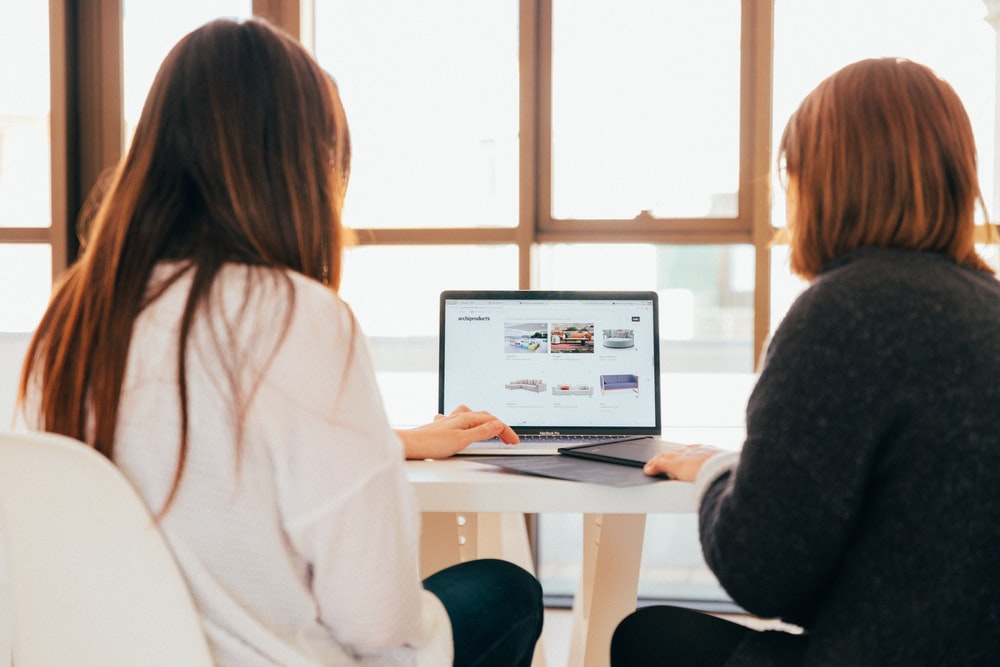 two women sit a table looking at a laptop