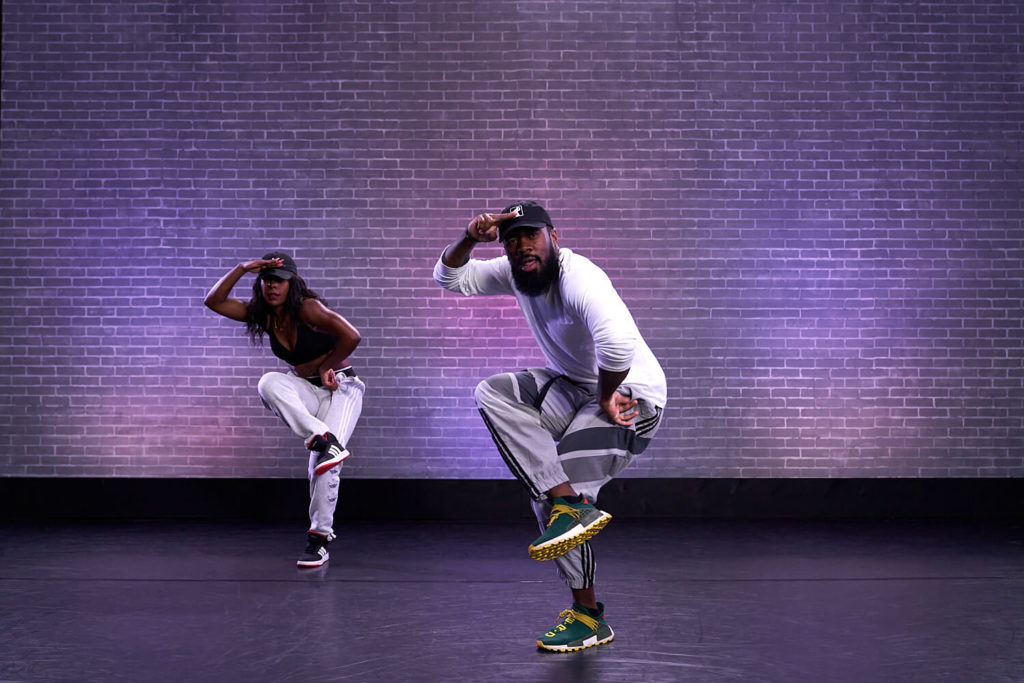 Two hip-hop dancers posing cross-legged in front of a purple background at cli studios.