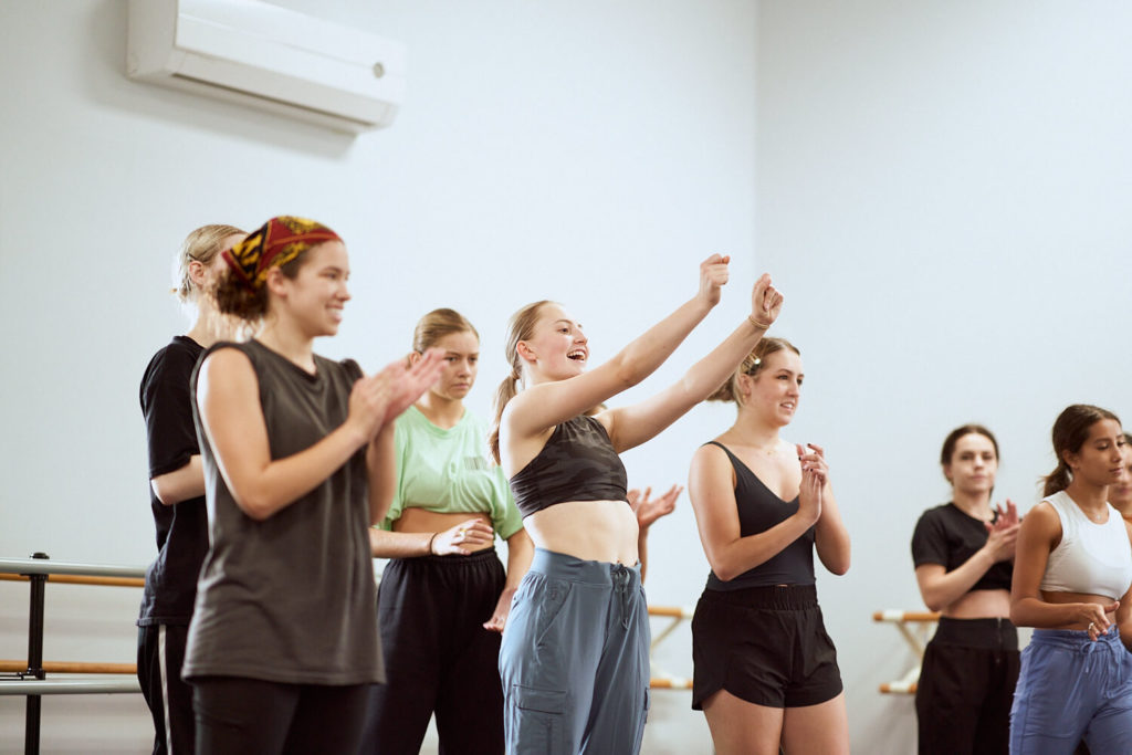 A group of CLI Conservatory dancers cheering and snapping their fingers in a dance studio 