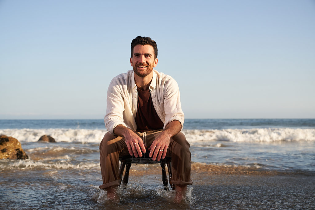 Teddy Forance sitting on a chair at the beach in wake of waves