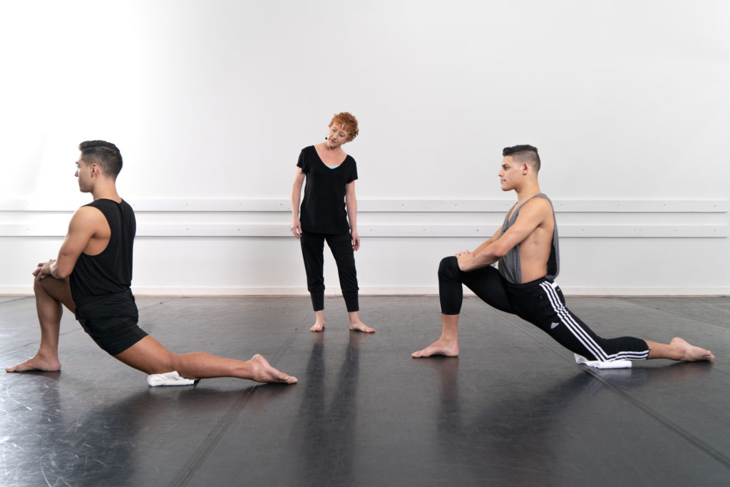 Two dancers stretching while an instructor coaches them