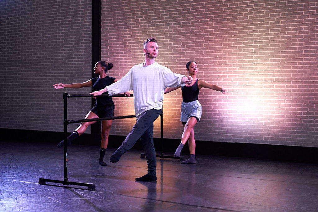Spenser Theberg at ballet barre with two female dancers with leg extended  and pointed in front with arm extended in second position