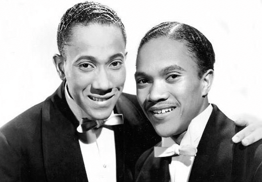 Black and white portrait of the Nicholas Brothers; two African American men smiling in suits and bow ties