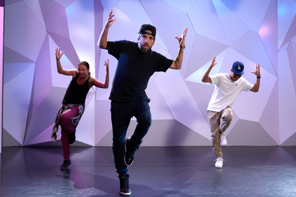 Marty Kudelka dances with two other dancers at CLI Studios. Dancers have their arms up and are standing on one leg