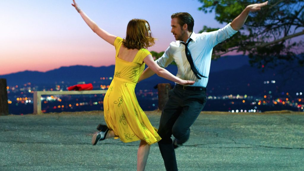 emma stone and ryan gosling in la la land a lovely knight with emma in yellow flowered dress and ryan in tie and pants dancing.