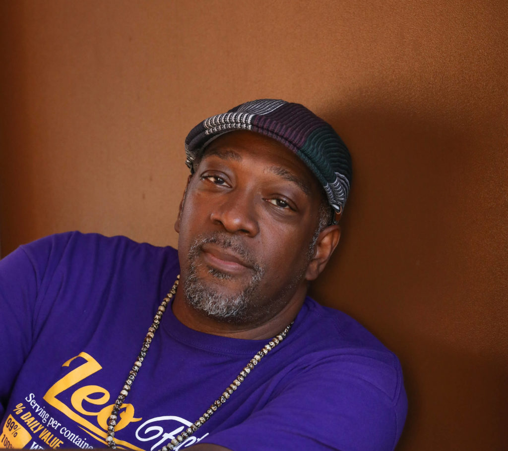 Moncell Durden portrait; man wearing a multicolored hat and gold chain