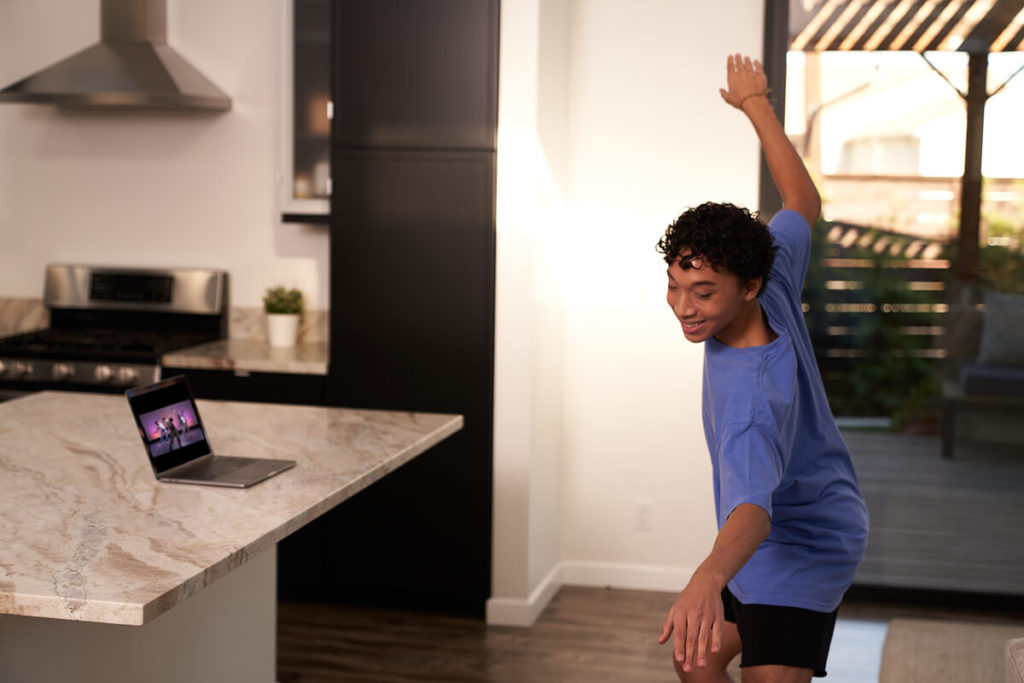 Dancer wearing a blue shirt taking a CLI Studios class at home in their kitchen with a laptop on the kitchen counter