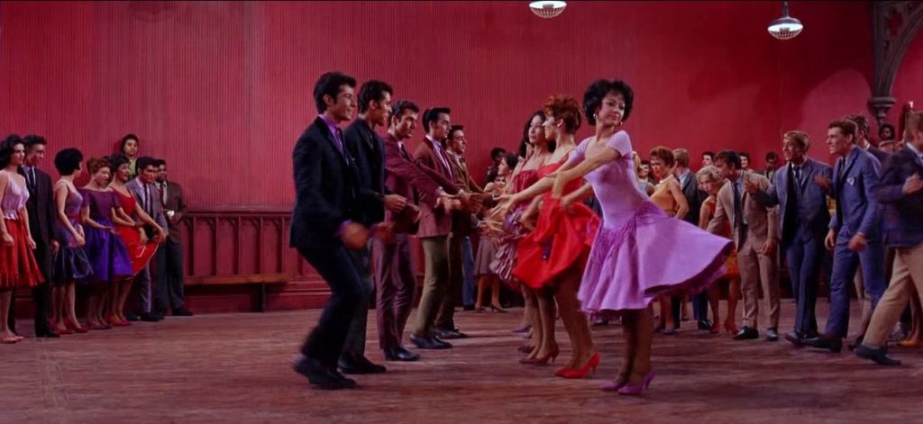 westside story dance scene in the gym with line of girls on the right in dresses and guys in suits on the left