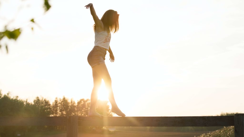 girl balancing outside with arms by her side on a fence in the sunset