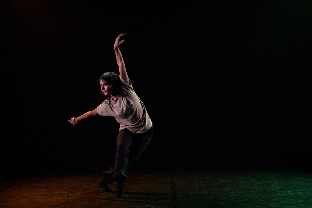 CLI Conservatory dancer with arms outstretched against a black background with green and red light in the foreground 