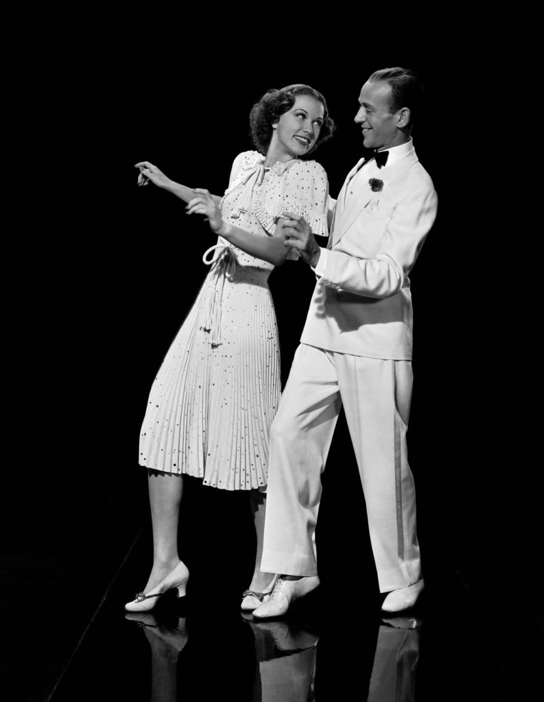 Eleanor Powell and Fred Astaire black and white dress and suit and bow tie, looking into each other’s eye’s while facing forward in a dance step