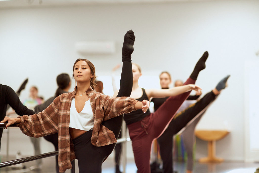 CLI Conservatory students at ballet barre with leg extended in second position and arm extended out to the side.