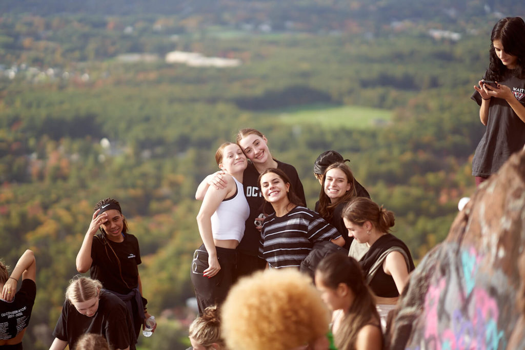 Girls from the CLI Conservatory smiling and hugging on top of a mountain with trees in the background 