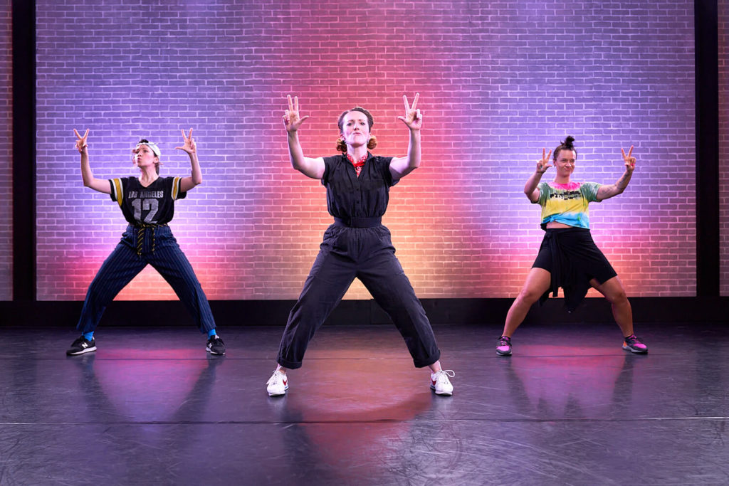 The Seaweed Sisters teaching dance at CLI Studios, all three women pose with three fingers up on each hand, with bent legs and goofy facial expressions