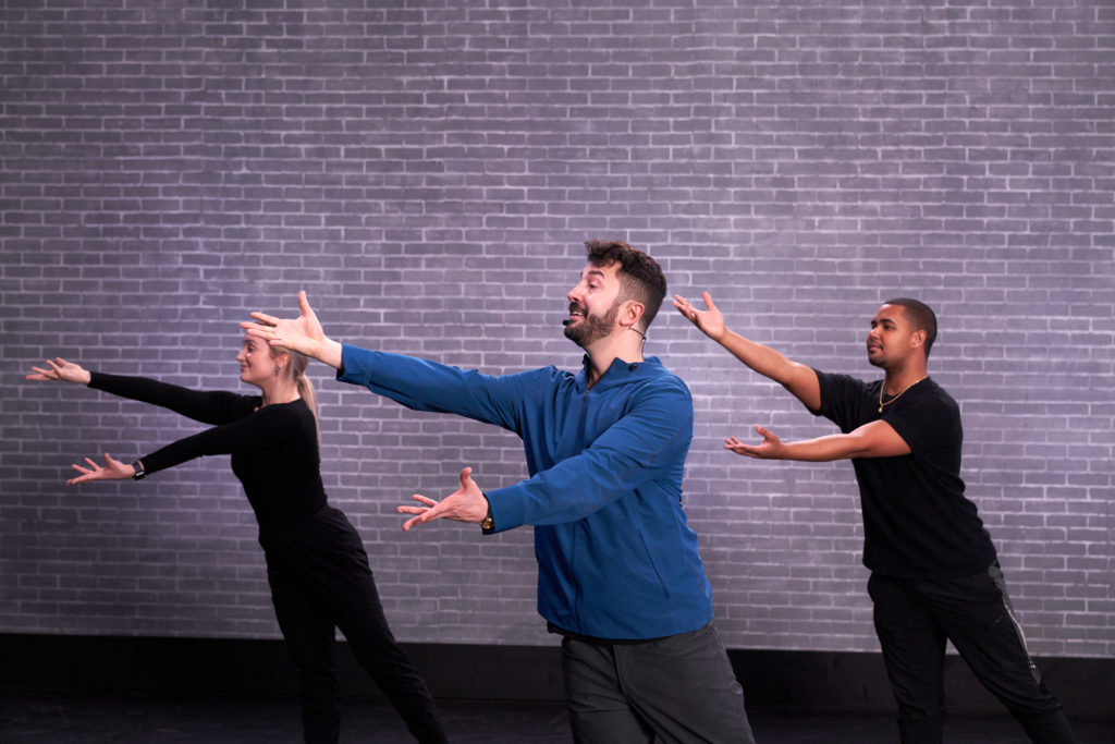 Al blackstone with 2 other dancers in black reaching to the left with both arms extended at CLI Studios.