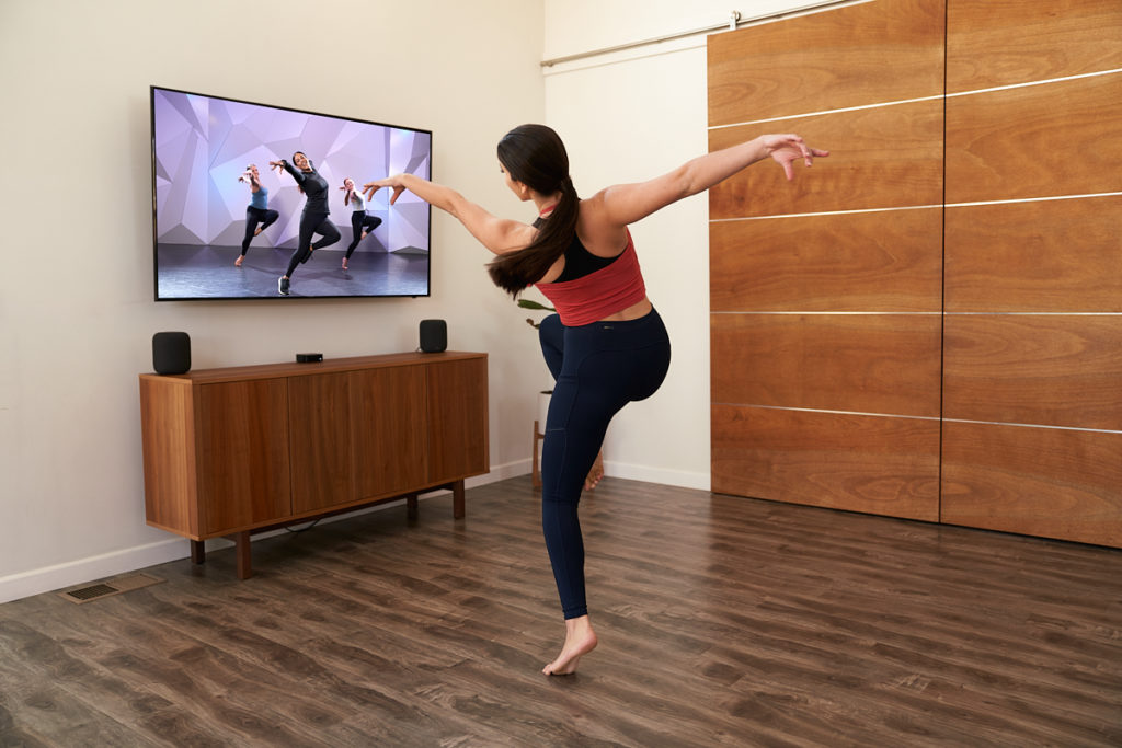 female dancer at home with foot in passe copying the dancer on her tv screen